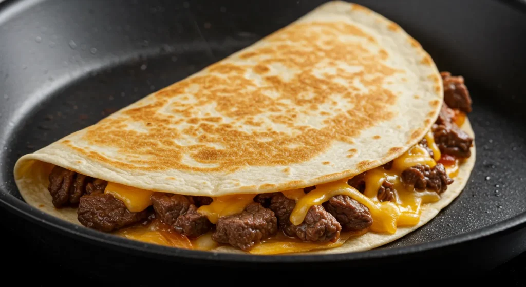 Cooking a folded cheesy beef quesadilla in a skillet until golden and crispy.
