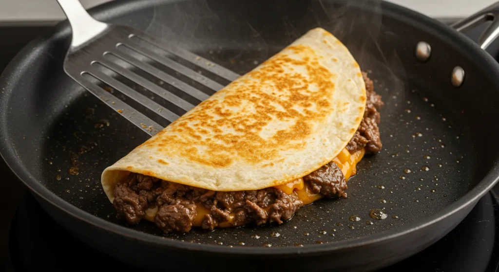 Flipping a homemade beef quesadilla to cook the other side until perfectly crispy.