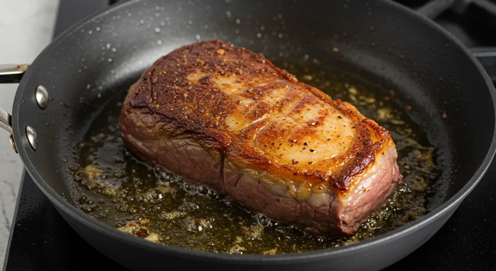 Seared tri-tip roast in a skillet, developing a golden-brown crust.